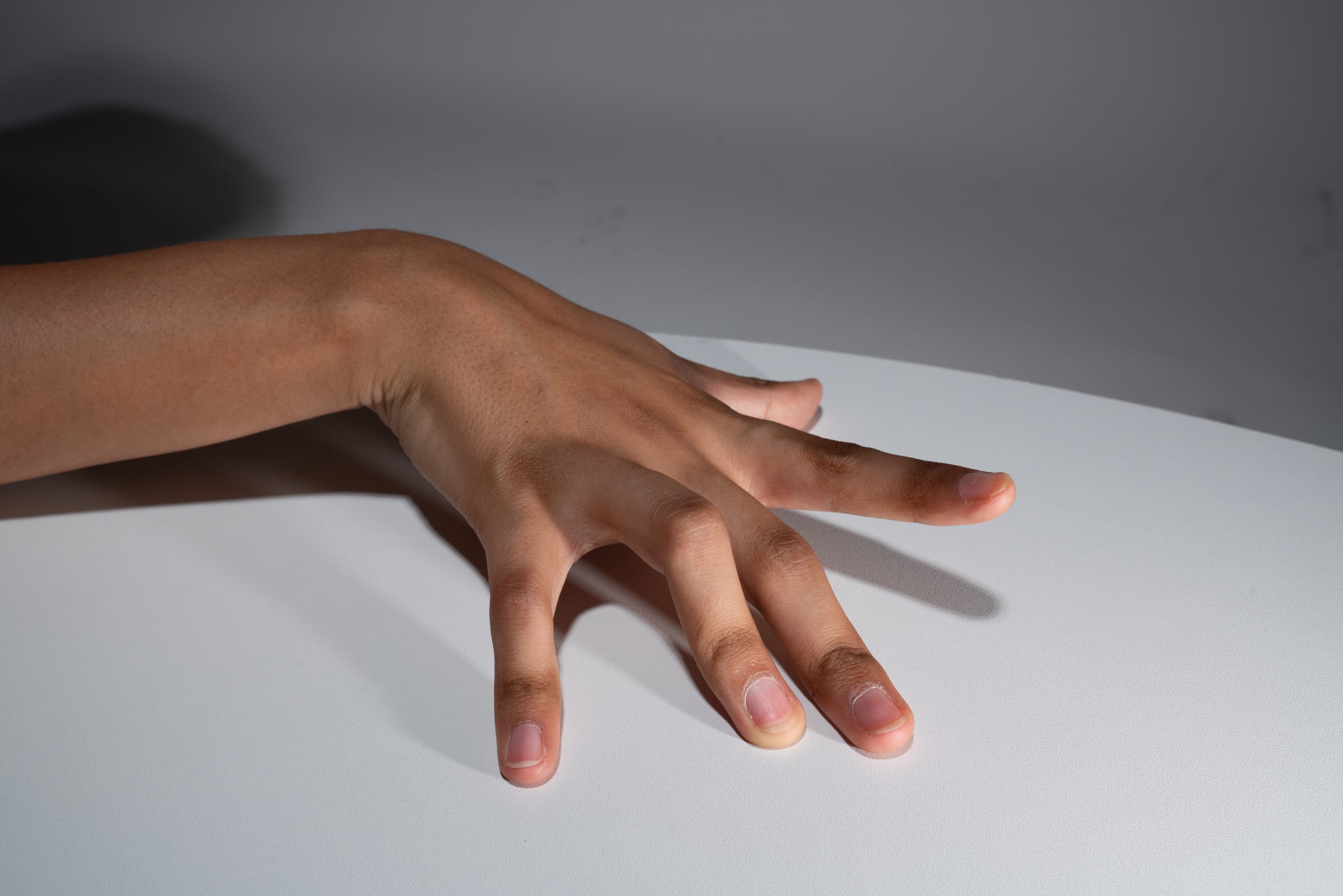 a close up image of a child's hand with tan skin, resting on a white table. the fingers are slightly spread apart. the image is lit with artificial light.