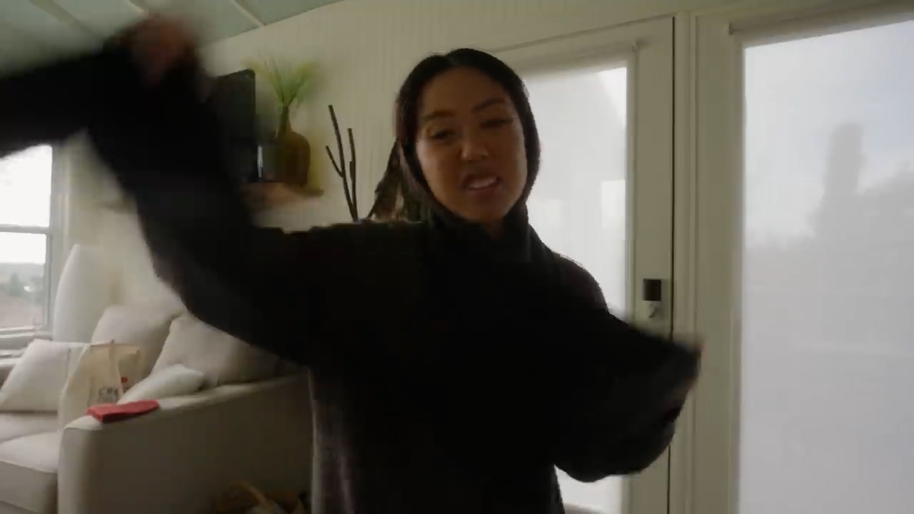 a young woman is captured middance inside a brightly lit home. she's wearing a black longsleeved top and appears to be caught in a moment of joyful movement. the room features a neutral color palette with a comfortablelooking couch and a glimpse of outdoor light through a window.
