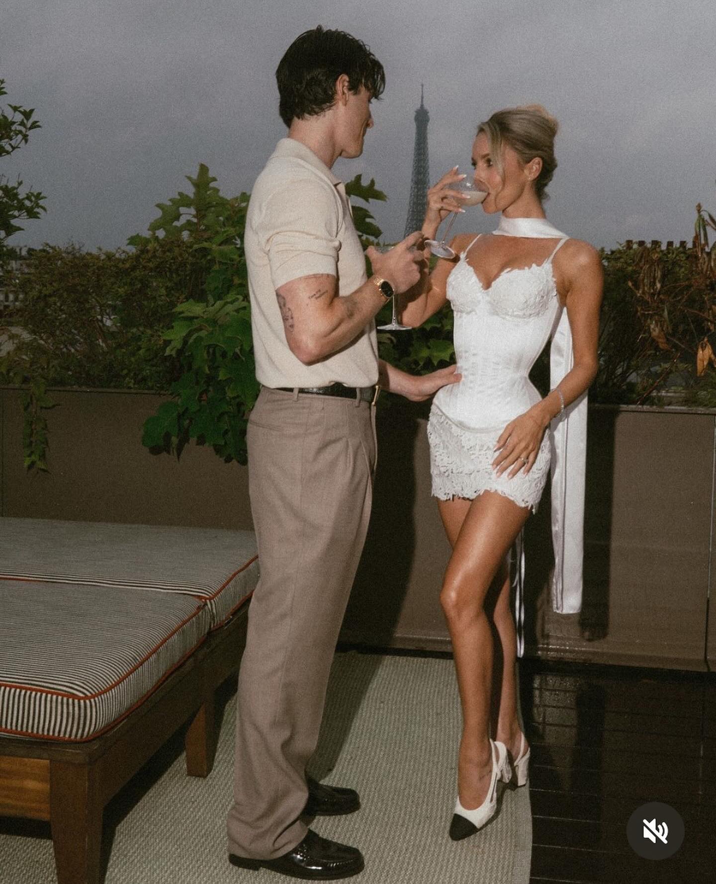 a couple in love is enjoying a romantic evening in paris. the man is dressed in a white shirt and brown trousers, while the woman is wearing a beautiful white dress with lace detailing and high heels. they are standing on a balcony overlooking the city, with the eiffel tower in the background. they are both smiling and toasting with champagne glasses, enjoying their special moment together. the image captures the beauty and romance of paris, and the joy of being in love.