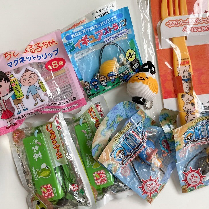 this image shows a collection of various packaged goods, including snacks, cartoon character merchandise, and promotional items. there are packages of japanese snacks, items featuring anime characters, and toys. there is also a set of utensils including a spoon and fork with cartoon characters.