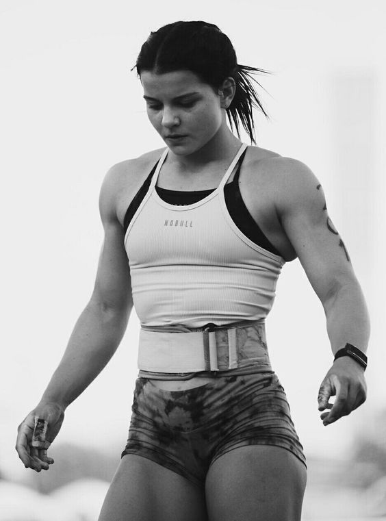 a black and white image of a female athlete.  she is muscular and wearing workout attire including a weightlifting belt.  she appears to be at a competition.