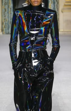 a model wearing a black iridescent leather jacket and black leather pants poses on a runway.