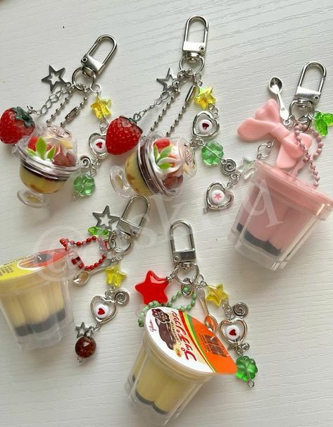 the image shows five keychains with foodthemed charms. two of the keychains feature a dessert in a small glass with a strawberry on top. one keychain has a pink container charm with a pink bow and spoon charm. the other two keychains have pudding container charms with various star, heart, and clover charms. all keychains have a silver clasp and chain.