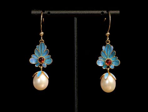 this is a photo of a pair of vintage earrings with a floral design. each earring features a blue enamel flower with a small orange stone at its center, dangling above a white pearl. the earrings are suspended from gold hooks. the backdrop is a solid black color.