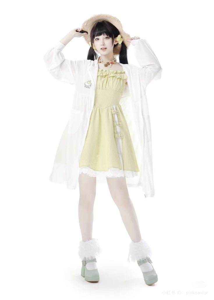 a young asian woman dressed in a pastel yellow dress with a white overcoat and a straw hat poses on a white background. she wears white stockings and light green mary jane shoes with fluffy white accents around the ankles. she has black hair styled into pigtails, fair skin, and a necklace. her dress has ruffles at the top and decorative chinesestyle knots on the side. she is holding the brim of her hat with both hands. the outfit evokes a lolita fashion style.