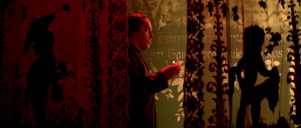 a man in silhouette, illuminated only by the warm glow of a lighter, stands between two heavy curtains. the curtains feature intricate patterns and the shadows of children at play, adding a layer of mystery and intrigue to the scene. the overall atmosphere is dark and dramatic, hinting at a sense of secrecy or suspense.