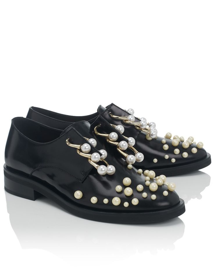 the image shows a pair of black leather women's oxford shoes adorned with numerous offwhite pearls. the pearls are strategically placed along the laces and across the shoe's vamp, creating a visually striking effect.  goldtoned hardware accents complement the pearls. the shoes are positioned on a clean white background, showcasing their detail and elegance. one shoe is slightly angled to reveal the sole and full design. the lighting is bright and even, emphasizing the texture and shine of the leather and pearls.