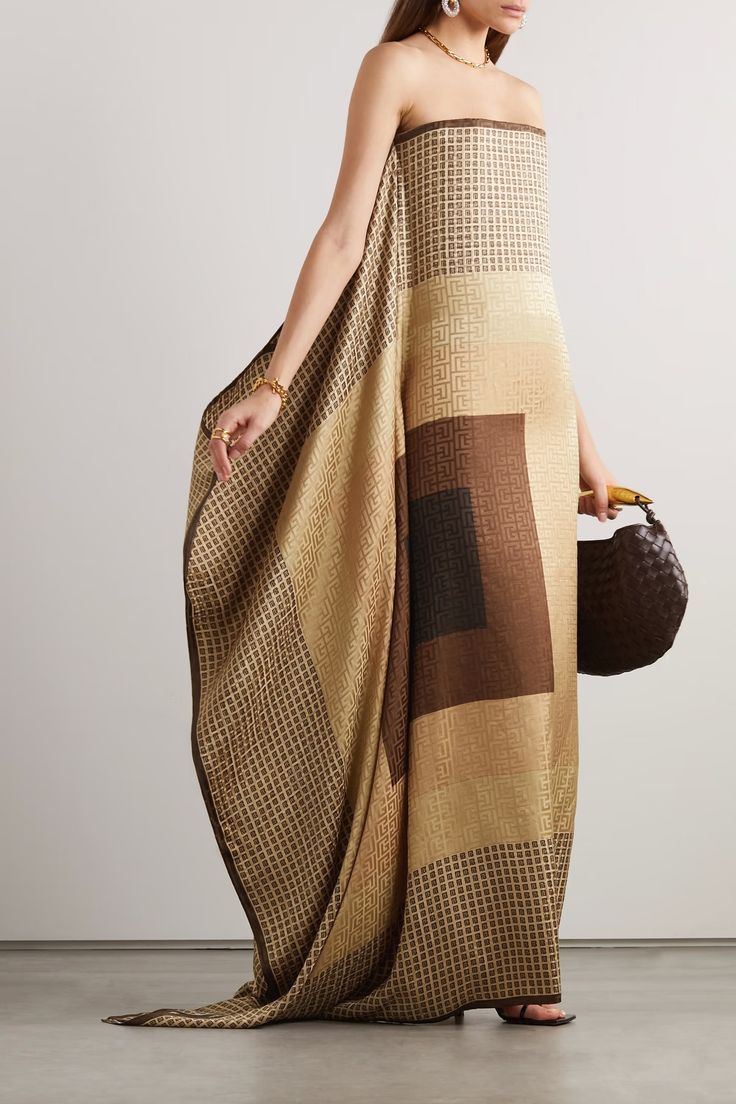 a woman is wearing a strapless, patterned dress in shades of brown and gold, accessorized with gold jewelry, and carrying a dark brown handbag.