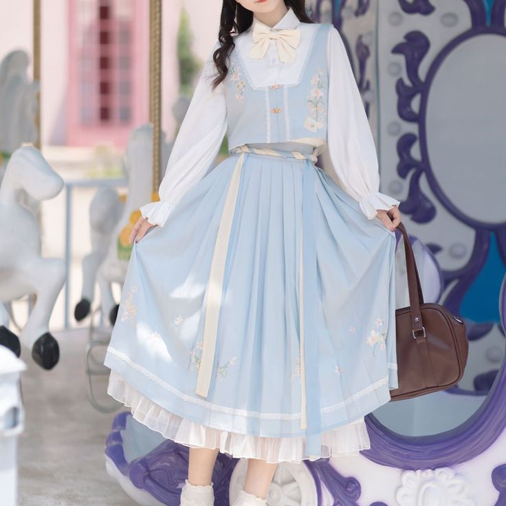 a young woman wearing a light blue lolita dress with white embroidery and a white blouse. she is standing in front of a carousel.