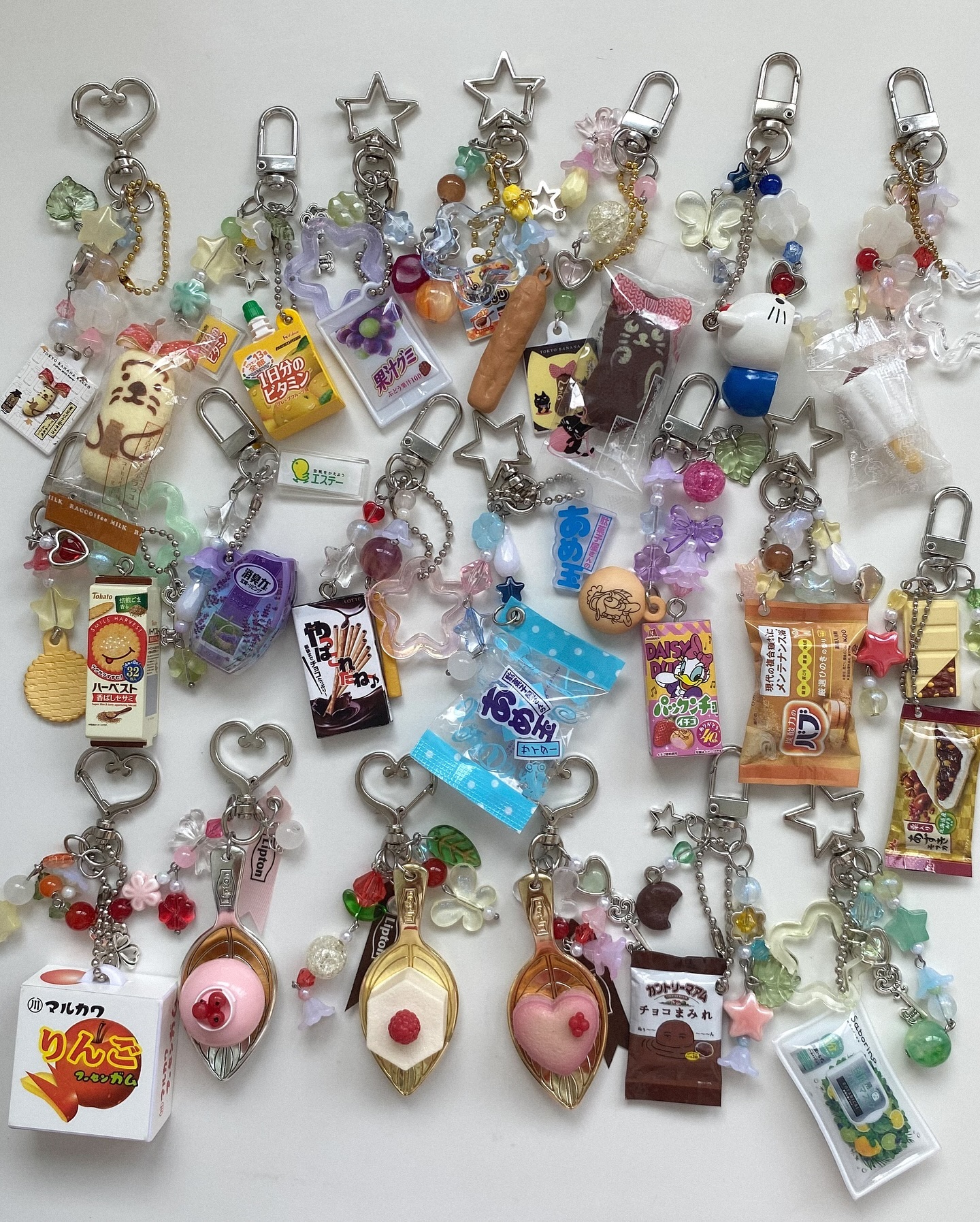 the image shows a collection of keychains with charms resembling miniature versions of various food, snacks, sweets, and beverages. the charms include items like juice boxes, chocolate sticks, biscuits, gum, chocolate, and candies. the keychains are arranged on a white background.