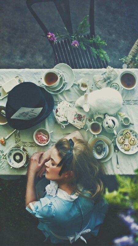 this image is a whimsical take on a tea party, possibly inspired by alice in wonderland. a young girl in a blue dress sits at a table covered in a white tablecloth and china teacups and teapots, as well as other objects like a white rabbit and a mad hatter's hat. the image is full of charming details and has a dreamlike and magical quality.