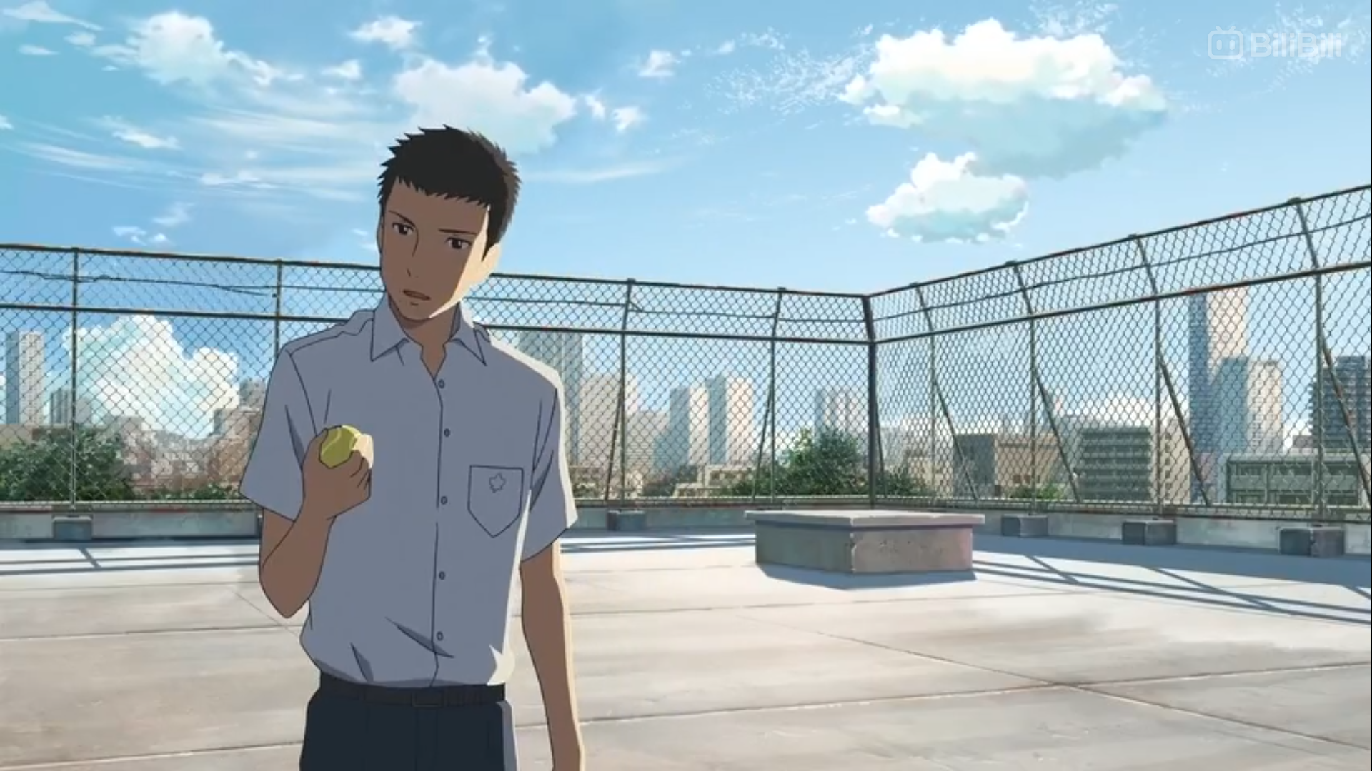 a young, animated boy in a school uniform stands on a rooftop. he holds a tennis ball in his right hand. he is facing left and looking slightly offcamera. behind him is a chainlink fence and a cityscape under a blue sky with some clouds.