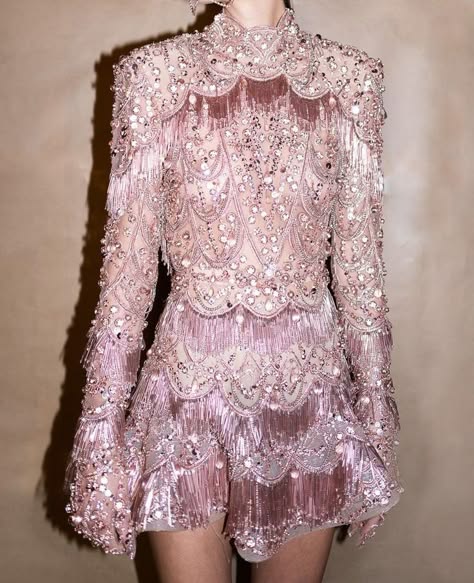 a woman is wearing a pink dress with sequins and fringe. the dress is very sparkly and glamorous, and the woman looks elegant and stylish.