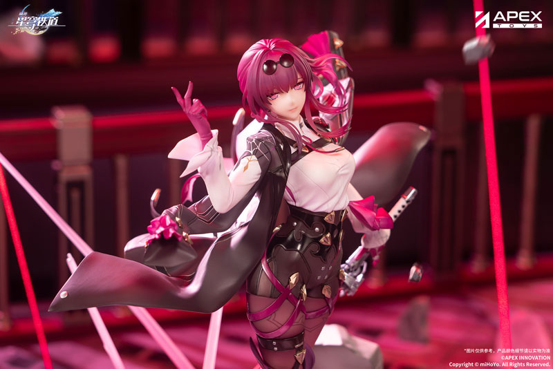 the image shows a detailed anime figurine of kafka from honkai: star rail, made by apex toys. the figurine is striking with its pink hair and a mix of black, white, and pink attire. she's posed dynamically, holding a swordlike object with pink embellishments. the background is a mix of soft focus and abstract elements, mainly in shades of red. at the top right, the apex toys logo is clearly visible. the figurine is placed on a textured surface, suggesting it's part of a display or promotional photoshoot. at the bottom of the image, there's a copyright notice indicating the rights belong to mihoyo.