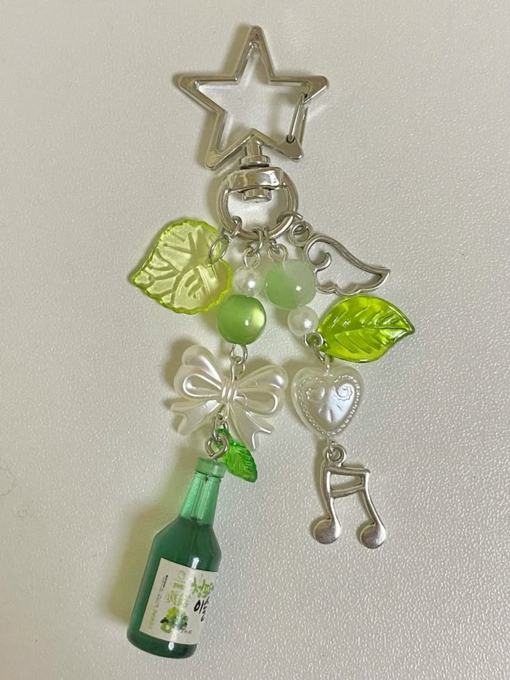 a closeup shot shows a keychain made of several trinkets, including a starshaped clip, leaves, beads, a bow, a wing, a heart, a music note and a green bottle.