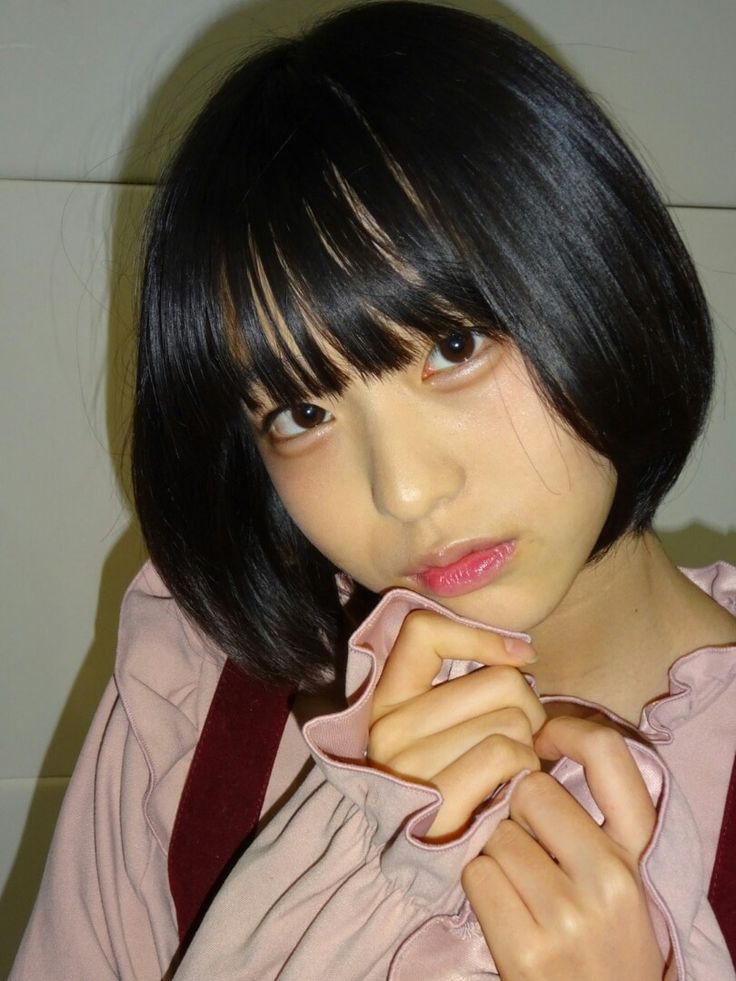a young asian girl with black hair and a white collar ruffles shirt, posing for a candid portrait in a casual studio setting. the girl has a soft, gentle expression on her face and is looking directly at the camera. she is wearing a pink shirt with a white collar and ruffles. the background of the photo is white.