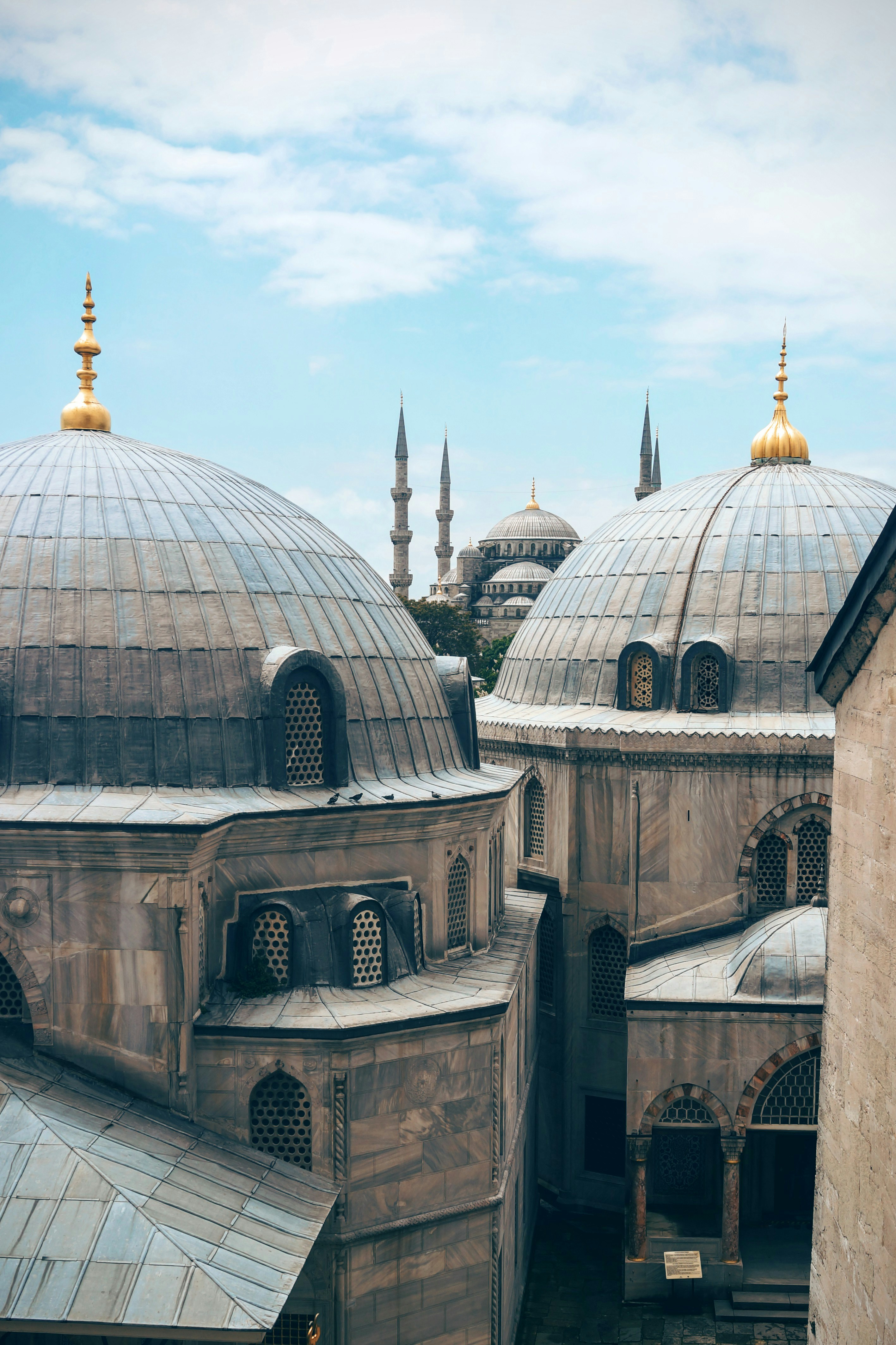 the image shows a part of the exterior of a mosque with the hagia sophia in the background. the domes and minarets of the mosque are visible, and the sky is blue with some clouds.