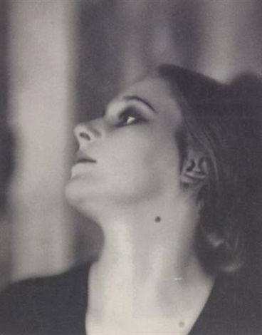 the image is a striking black and white portrait of a woman.  her head is tilted upwards, her gaze directed towards an unseen point above.  the lighting is dramatic, using chiaroscuro to highlight the contours of her face and neck. the soft shadows and highlights give the photograph a timeless, almost ethereal quality. the woman's expression is contemplative and mysterious. her hair is styled in a manner suggestive of the 1920s or 1930s. the overall aesthetic is elegant and sophisticated, reminiscent of vintage fashion photography or art deco style. the background is blurred and out of focus, drawing attention to the subject.
