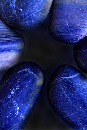 a macro shot of six polished blue stones laid out on a dark background, capturing their smooth texture and intricate patterns. the contrasting shades of blue and the glistening surface create a visually captivating image, highlighting the beauty and uniqueness of natural gemstones. the overall feel is both abstract and natural, evoking a sense of serenity and wonder.