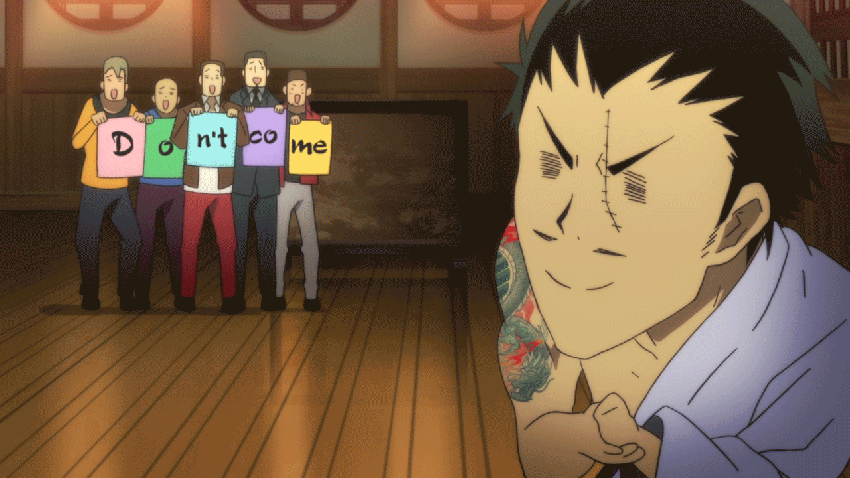a group of men in colorful sweaters stand in a line holding up signs that read "don't come". a shirtless, smirking man with tattoos stands in the foreground. he appears to be the subject of their fear and the recipient of their message. the scene is brightly lit and appears to take place indoors, likely in a home or dojo. the perspective is at eye level.