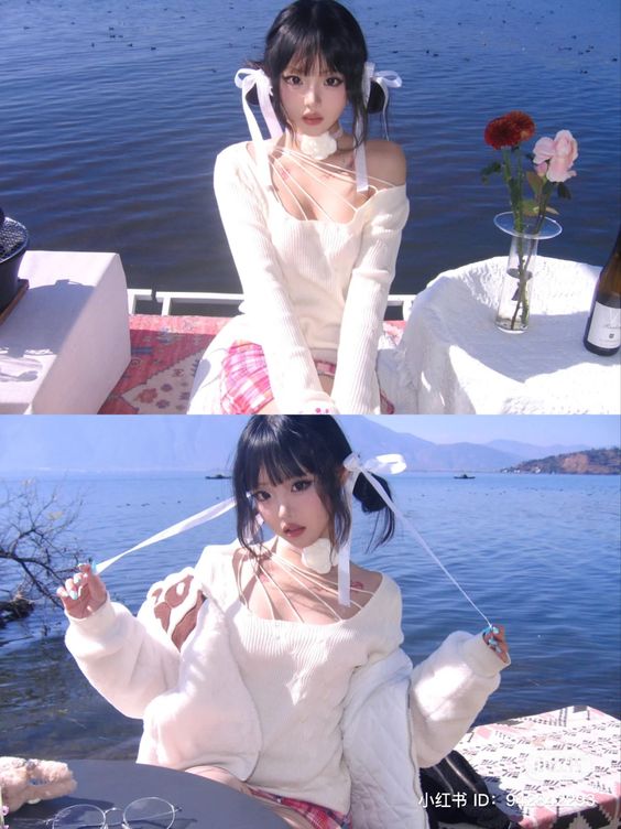 a young woman with black hair styled with white ribbons poses on a dock by a lake. she is wearing a white offshoulder sweater and a pink plaid skirt. there is a picnic set up on the dock with a vase of roses. the background is a serene blue lake and clear sky. the image is brightly lit by natural sunlight.