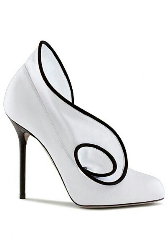 a single white high heel shoe with black trim is presented against a blank white background. the shoe has a unique design with a curved upper and a slim, high heel.