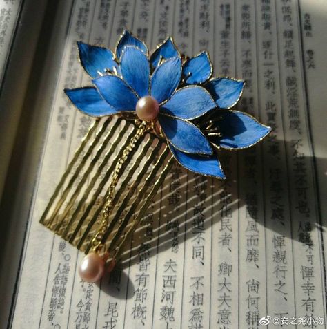 a gold hair comb adorned with delicate, blue lotus flowers and pearls rests upon a page of a chinese book. the image is bathed in warm, natural light, highlighting the intricate details of the comb and the elegant script of the text.