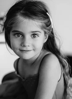 a black and white portrait of a young girl with long hair and a hair clip. she is looking directly at the camera with a gentle smile.