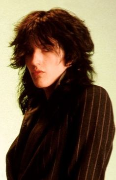 a portrait of a woman with long dark hair, wearing a pinstripe blazer. the woman is looking directly at the camera, with a serious expression. the background is a light neutral color.