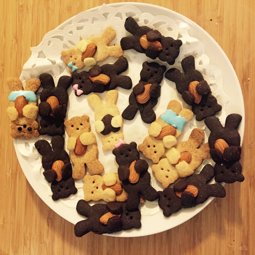 the image shows a plate of teddy bearshaped cookies. some of the cookies are chocolate flavored and some are plain. each cookie is decorated with an almond slice.