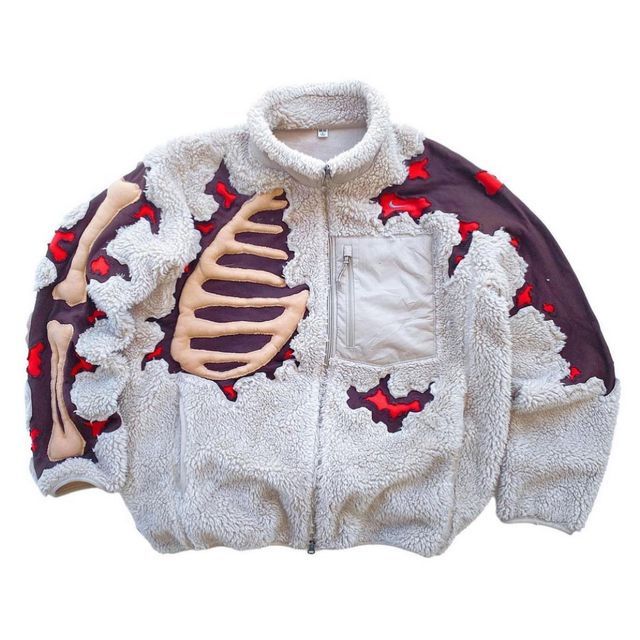 a white fleece jacket with a skeleton design, red blood splatters, and brown patches. the jacket is zippered up the front and has a large pocket on the left side. the jacket is warm and comfortable and perfect for casual wear.