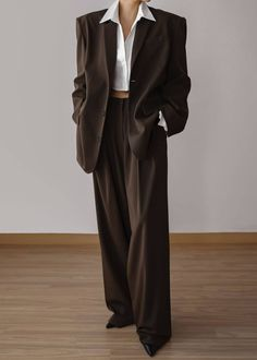 a woman is wearing a brown blazer and pants suit. she's posing for the camera with a white shirt peeking out from under the blazer. her outfit is stylish and professional.
