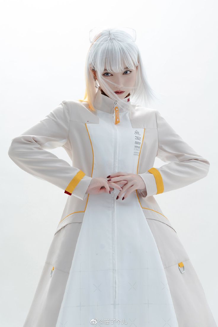 a young woman with white hair is wearing a white coat with yellow accents. the coat is long and flowing, with a zipper down the front. she is standing with her hands clasped in front of her, and she is looking directly at the camera with a serious expression.