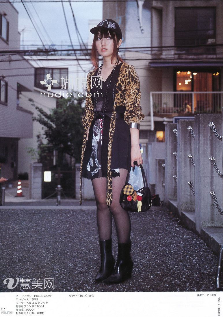 a young woman is posing on a sidewalk in an urban setting for a fashion magazine spread. she's wearing a leopard print cardigan, a black dress, black tights, black ankle boots, and a black baseball cap. she's carrying a black purse with a colorful design. the photo is welllit, taken from eye level, and showcases a trendy and edgy street style look.
