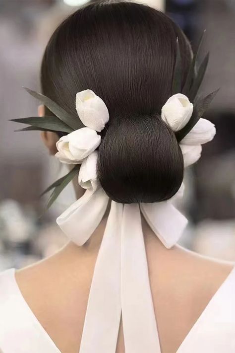 a bride with a beautiful white floral updo. the bride is wearing a white dress and is standing with her back to the camera. the hairstyle is sleek and elegant. the flowers are white tulips and they are arranged in a beautiful way to create a delicate and romantic look. the photo is taken from behind the bride, showing off her stunning hairstyle and her simple yet elegant white dress. the bride's back is beautifully sculpted and the white of her dress is a stark contrast to her dark hair. the photo captures the bride's beauty and the essence of a bridal updo.  it's a perfect example of a modern and timeless wedding hairstyle.
