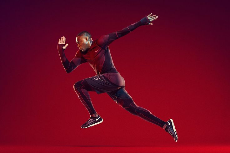 an athletic male runner in black nike sportswear jumps midair against a red background.  his body is positioned as if he is in the middle of a running stride.  the man's expression is focused and determined, demonstrating the strength and energy needed for a highintensity workout.  the red background enhances the dynamic nature of the image, emphasizing the athlete's speed and motion.