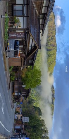 this is a photo of a street in a japanese town. the street is lined with traditional japanese buildings, and there are trees and mountains in the background. the sky is blue and there are some clouds in the sky. the photo is taken from a high angle. the photo has a peaceful and serene atmosphere.
