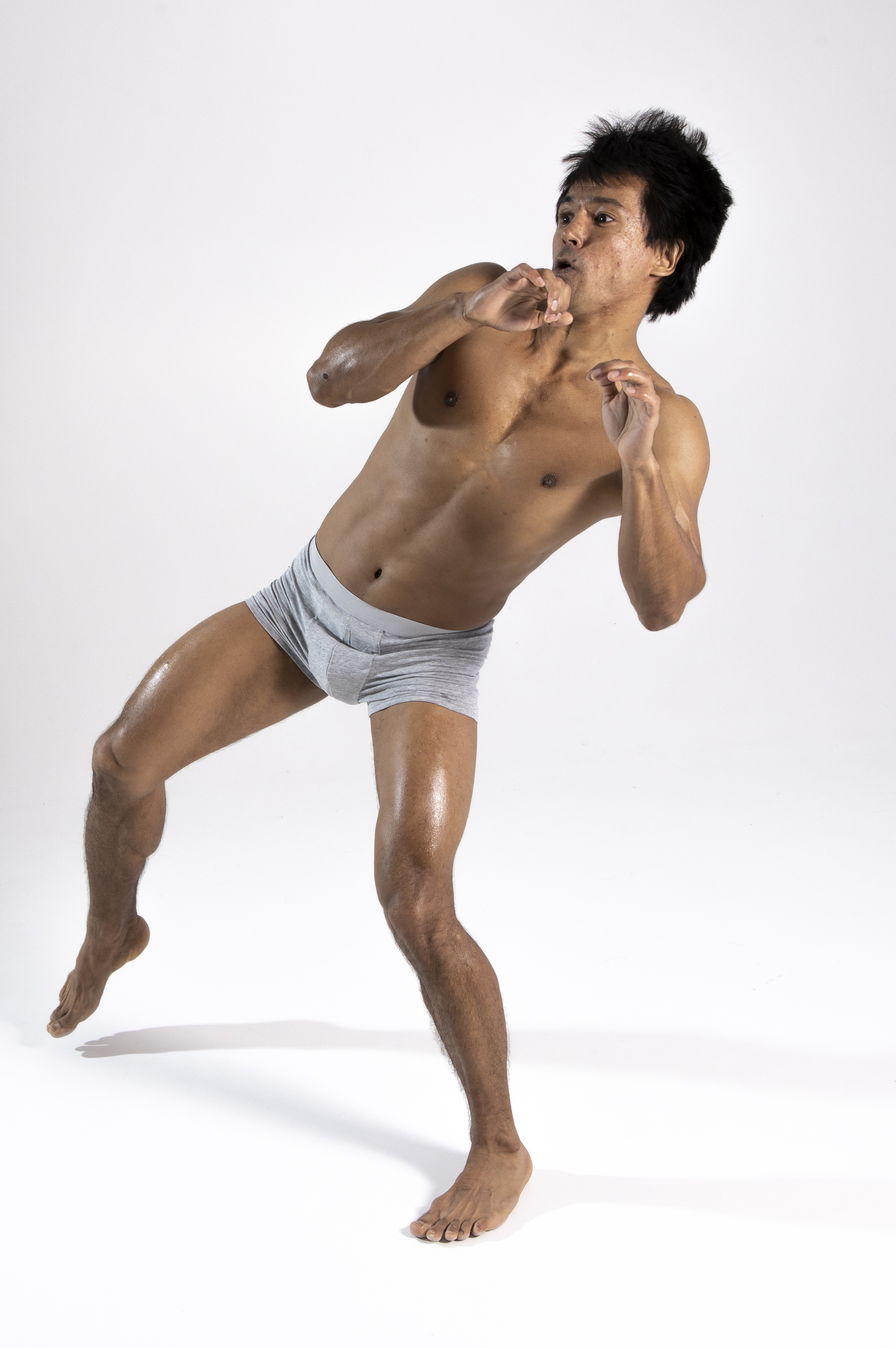 a shirtless, athletic asian man wearing boxer shorts is shown in a defensive stance against a white background. he is barefoot and his skin appears wet or glistening.