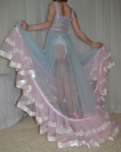 a woman in a pink and blue sheer lace dress with ruffles. the dress is very delicate and feminine. the woman is