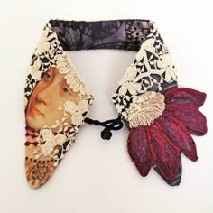 a closeup shot of a unique, handmade collar crafted from a variety of fabrics, including lace, velvet, and printed fabric. the collar features a flower motif and an ornate design. the piece has a vintage and bohemian aesthetic.