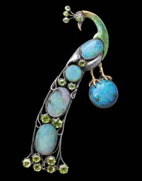 this is a photo of an art nouveau brooch in the shape of a peacock. the peacock is encrusted with opals and peridot. the peacock is holding a large opal in its claw.
