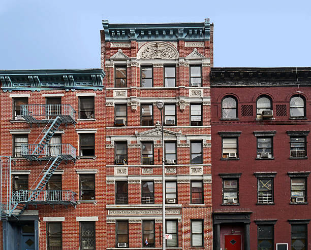 a classic new york city street view featuring the iconic brownstone buildings.  three buildings stand tall, showcasing intricate architectural details and the characteristic fire escapes. the warm brick facades, punctuated by numerous windows, hint at the bustling life within the urban dwellings.