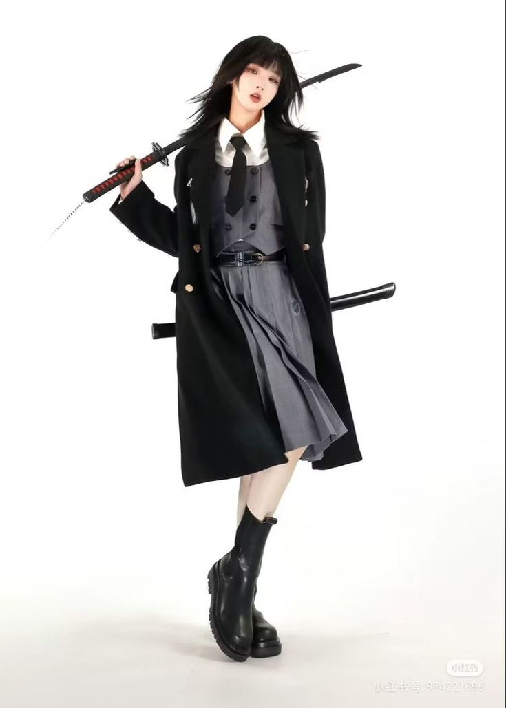 a young woman in a black coat and grey skirt is holding a katana sword. she is standing in a studio with a white background. she is wearing black boots.