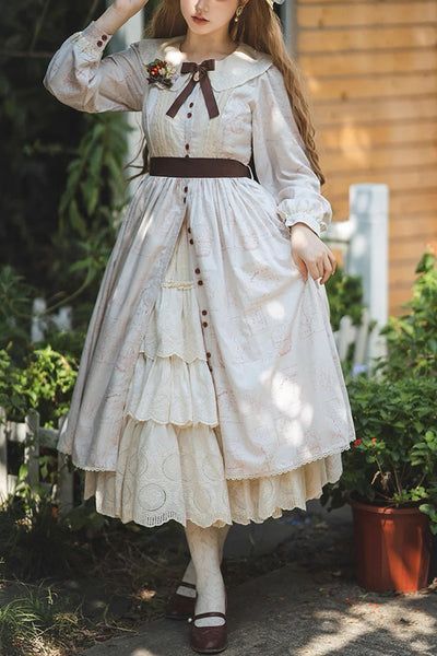 a young woman is standing outdoors, modeling a long, white dress with a brown bow and lace detailing. the dress falls to her shins and she is wearing brown mary jane style shoes. she is also wearing a white hat and has long, brown hair. the background of the image is a wooden building with some green plants in pots. the lighting is natural and sunny.