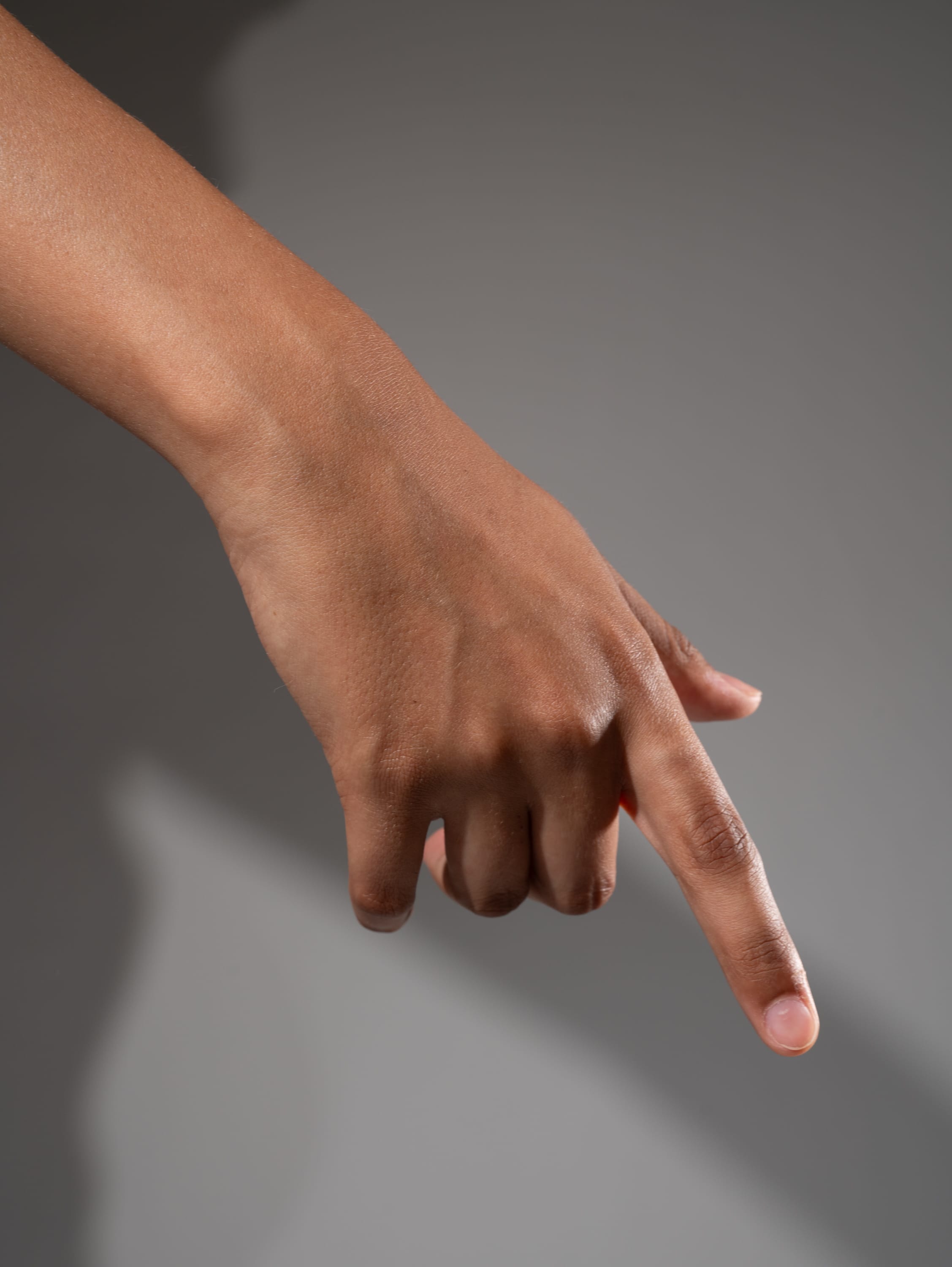 an image of a hand with a pointing index finger, isolated against a light gray background. the hand has a medium brown skin tone.