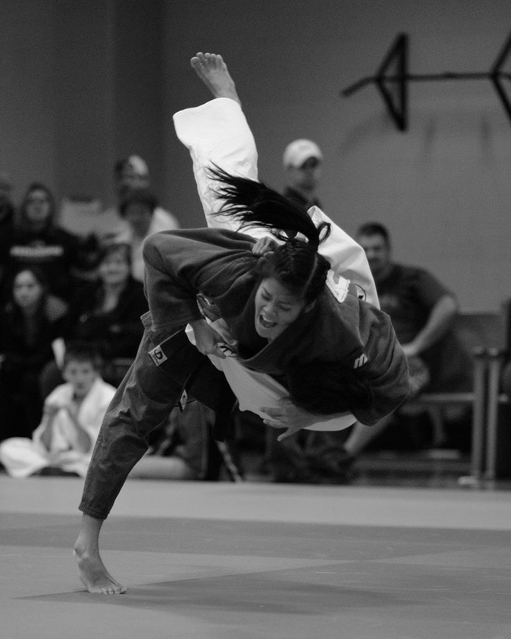 a black and white image of a female judo athlete in midair during a competition. she is in a dynamic pose, midthrow, showing the intensity and skill of this martial art. the image is a powerful depiction of the action and concentration required in judo.