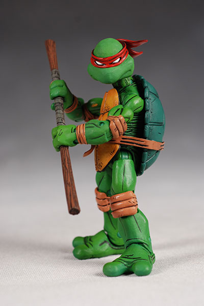 the image shows an action figure of raphael from the teenage mutant ninja turtles. he is green with a red mask and is holding a staff.