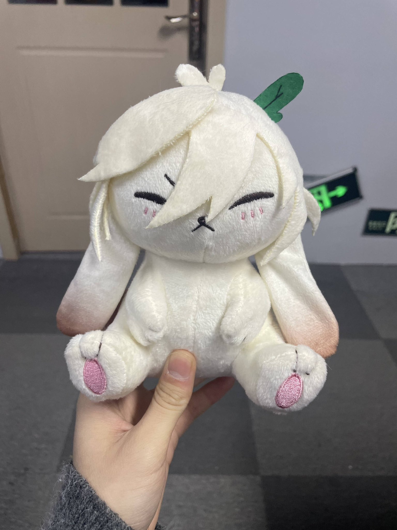 a white plush toy bunny with pink accents, a green leaf on its head, and a soft, fluffy texture is held in a person's hand. the bunny is a popular anime character and its cuteness is evident in its wide eyes and sweet expression.