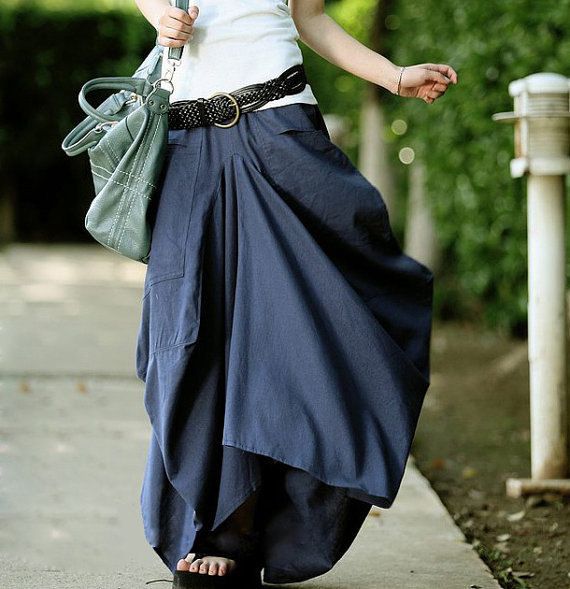 a woman is wearing a white top, a black braided belt, and a navy blue maxi skirt with a green handbag. she is wearing black sandals. she is standing on a sidewalk outdoors.