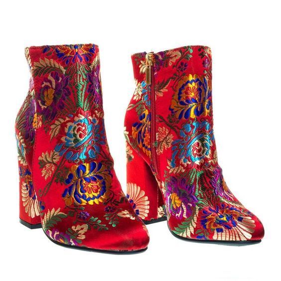 a pair of red ankle boots with block heels are displayed. the boots are decorated with an ornate floral pattern in various colors including blue, yellow, green, and purple. the boot on the right has a gold zipper running vertically along the side. both boots are isolated on a white background.